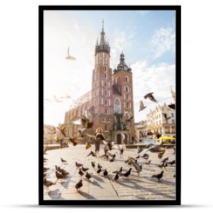 Widok na centralny plac i słynną bazylikę Mariacką z gołębiami latającymi podczas wschodu słońca w Krakowie