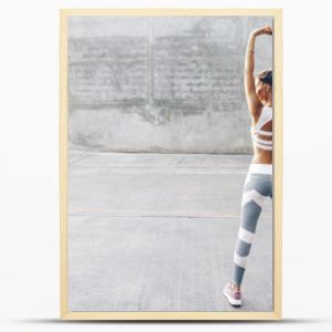 Kobieta uprawiająca sport fitness w modnej odzieży sportowej robi ćwiczenia rozciągające na szarej ścianie