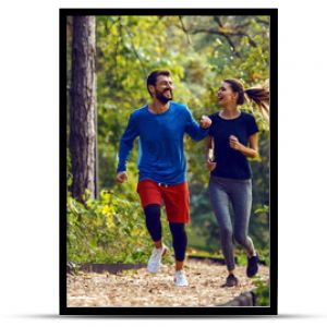 Pełna długość, dopasowana, sportowa, szczęśliwa para kaukaska w odzieży sportowej biegająca rano po lesie na szlaku