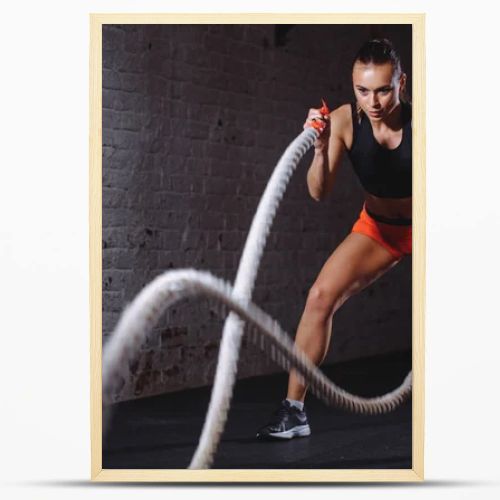 Battle ropes session. Attractive young fit and toned sportswoman training in gym