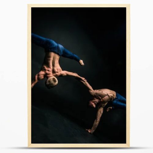 Male acrobatic duo performs a complicated balancing act on a dark background.