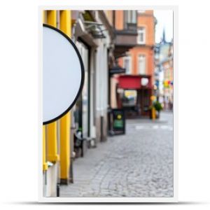 Blank round street sign on colorful cobblestone street in European town. Concept of travel, exploration, and urban signage.