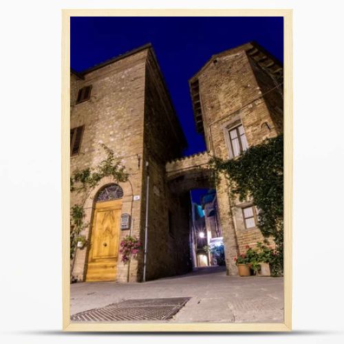 Little square of a small ancient Italian town, with brick houses, a wooden door and green and flowering plants. Journey to Tuscany and Umbria