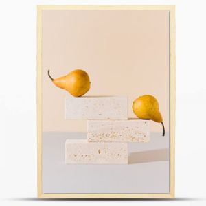 Golden yellow pears balancing on travertine marble blocks structure against gray and beige background. Creative gold summer fruit arrangement. Minimal retro styled surreal food art concept.