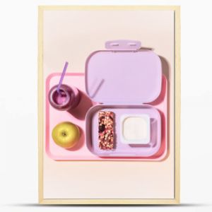 The concept of healthy school meals. Food composition with lunch box with yogurt, cereal bar, apple and oatmeal berries cocktail on a pink background with window light. Flat lay, horizontal banner