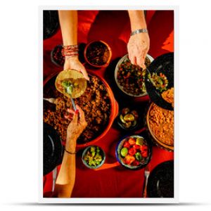 Overhead shot of a dinner table with Mexican food and hands. Tacos, beans, carnitas, habanero, salsa