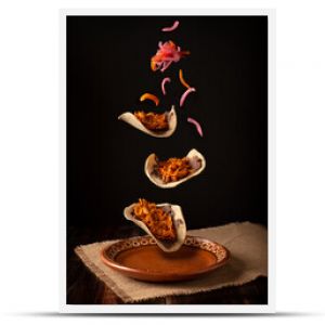 Creative food image of Mexican Tacos de Cochinita Pibil and onion with habanero chili falling on traditional mexican clay dish. Levitation photography.