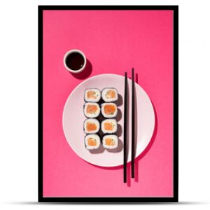 Japanese Sushi roll with salmon, cucumber and soy sauce with chopsticks in the plate on pink background with hard shadow. Concept food photography. Top view and copy space