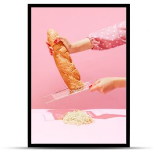 Female hands grating bread, baguette to make breadcrumb for meat isolated over pink background