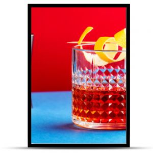 Sazerac, alcoholic cocktail drink with cognac, bourbon, absinthe, bitters, sugar and lemon zest. Dazzling red blue background with hard light and shadows pattern