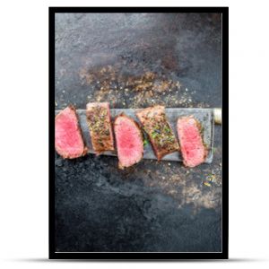 Traditional barbecue aged venison backstrap roast sliced with herbs as top view on a large knife with rustic background with copy space