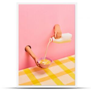 Food pop art photography. Female hands sticking out pink paper, pouring milk into bowl with corn flakes, ceral. Breakfast. Taste, creativity, art. Complementary colors. Copy space for ad, text