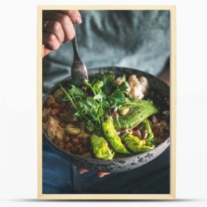 Healthy dinner or lunch. Woman in t-shirt and jeans eating vegan superbowl or Buddha bowl with hummus, vegetable, salad, beans, couscous and avocado