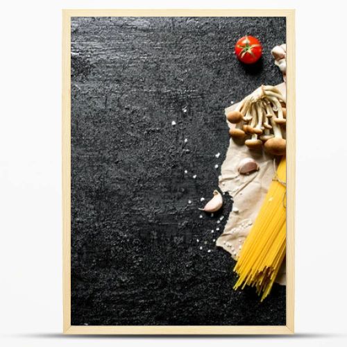 Raw spaghetti on paper with mushrooms, spices and tomatoes on a branch. On black rustic background