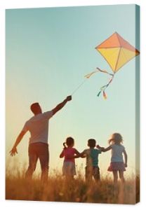 Father flying a kite with children in the field on sunlight sky