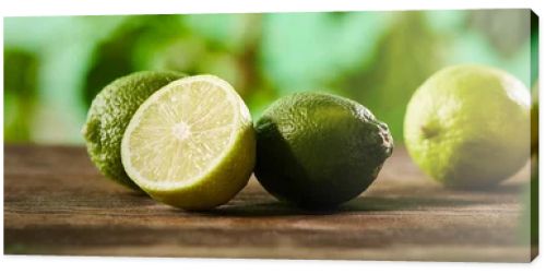 panoramic shot of cut and whole limes on wooden surface 