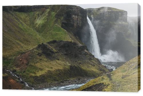 icelandic landscape with Haifoss waterfall and green hills on misty day