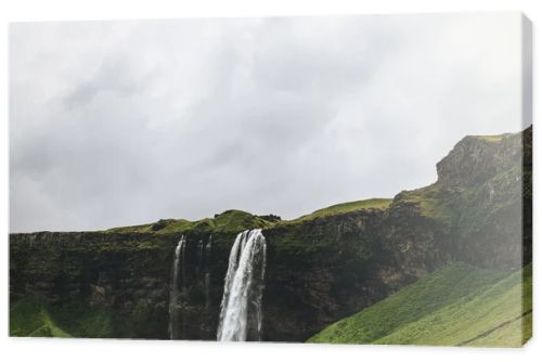 scenic view of landscape with Seljalandsfoss waterfall in highlands under cloudy sky in Iceland 