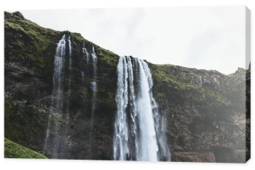 low angle view of Seljalandsfoss waterfall in highlands under cloudy sky in Iceland 