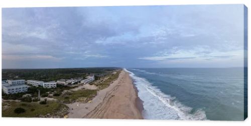 Drone panorama of Napeague on Long Islands South Fork, showing Atlantic Ocean surf, sandy beach, dunes and a beachfront resort complex at dusk.