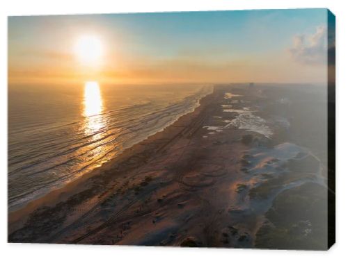Cinematic 4K aerial drone footage captures Miramar Beach dunes at sunrise in Ciudad Madero, Tamaulipas. Warm orange and golden light paints the sky and reflects on the calm sea as the coastline stretches to the horizon. Palapas line the shore while A