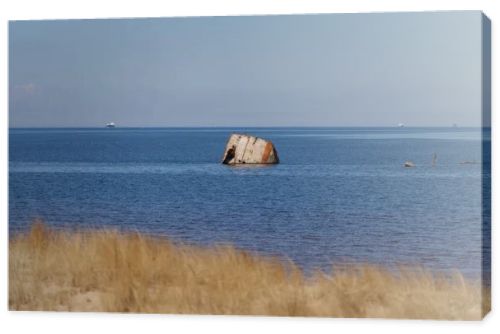 Rusted shipwreck fragment rising from calm sea beyond sandy dune grass, coastal decay, maritime history and Baltic shoreline landscape concept