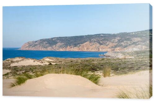 Sandy dune landscape with a wooden coastal path and distant rocky cliffs along the Atlantic coast near Guincho Cascais Portugal.