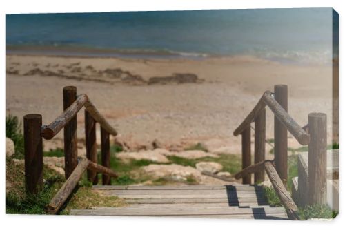 Wooden boardwalk with railings leading to a quiet sandy beach and turquoise Mediterranean sea. Sunny coastal scene with clear blue sky and peaceful vacation atmosphere.