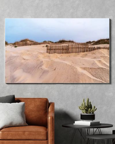A sandy dune landscape with wooden fences lines the edge of a beach under an overcast sky. The scene captures the raw beauty of a coastal environment with a serene and untouched atmosphere.