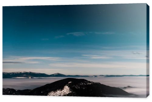 scenic view of snowy mountains with pine trees and white fluffy clouds in dark sky in evening