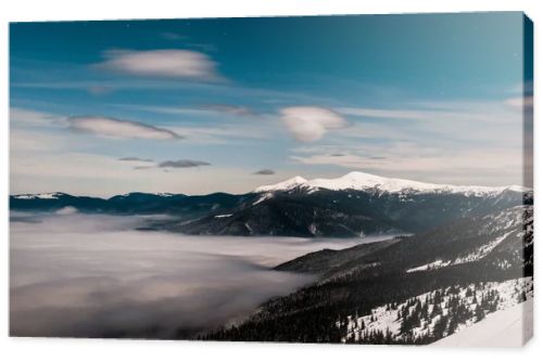 scenic view of snowy mountains with pine trees and white fluffy clouds in dark sky in evening