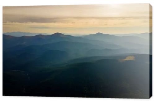 Aerial view of dark mountain hills with bright sunrays of setting sun at sunset. Hazy peaks and misty valleys in evening.