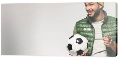 Smiling sportsman with football pointing with finger at camera isolated on grey, banner 