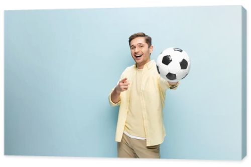 happy man in yellow shirt pointing with finger and holding football on blue