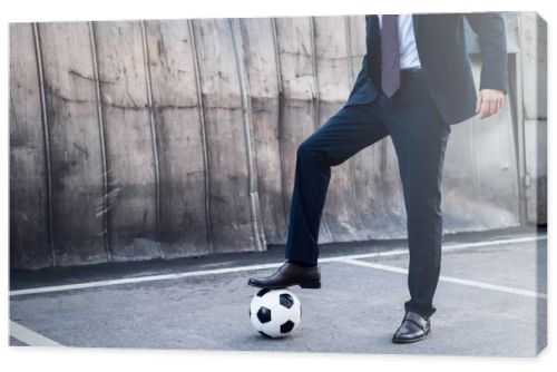 partial view of businessman in suit playing soccer on street