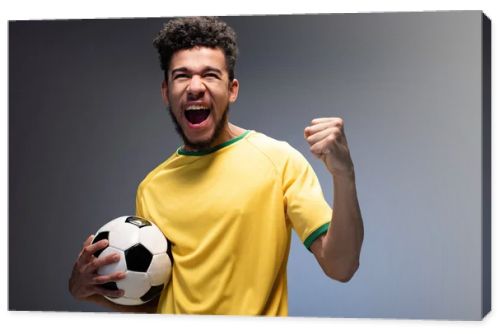 excited male african american football fan in yellow t-shirt holding ball on grey