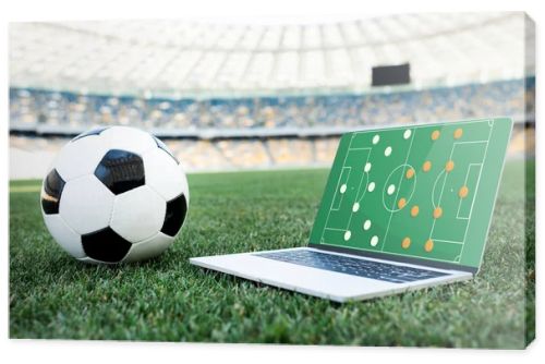 soccer ball and laptop with formation on screen on grassy football pitch at stadium