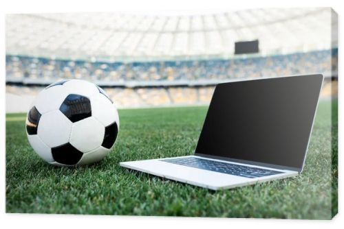 soccer ball and laptop with blank screen on grassy football pitch at stadium