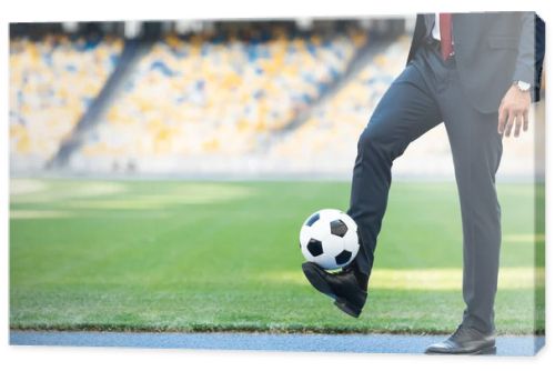 cropped view of young businessman in suit playing with soccer ball at stadium