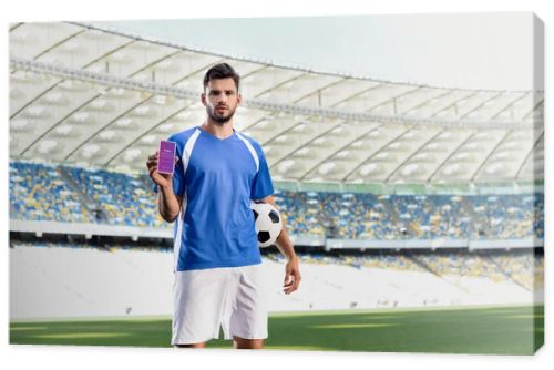 KYIV, UKRAINE - JUNE 20, 2019: professional soccer player in blue and white uniform with ball showing smartphone with Instagram app at stadium