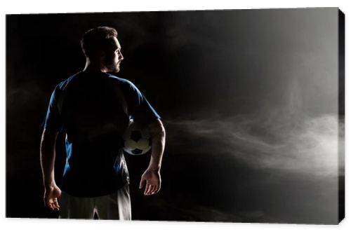 silhouette of football player holding ball on black with smoke  