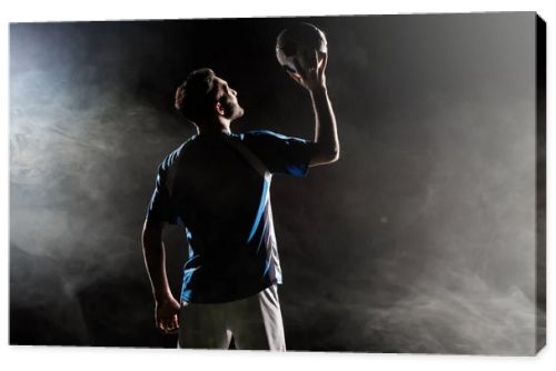 silhouette of player in uniform holding ball above head on black with smoke  