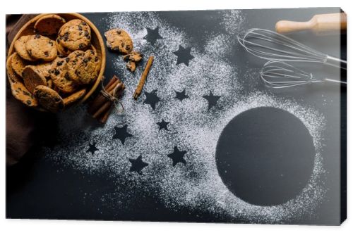 view from above of cookies in bowl, whisks and rolling pin on table covered by flour with symbol of stars