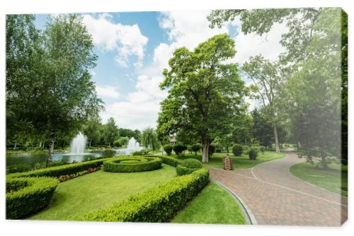 walkway near green plants, trees and fountains against blue sky 