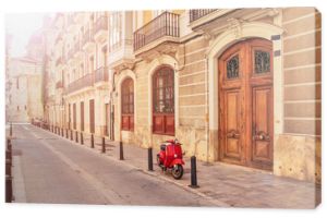 Spain. Valencia. A street in the tourist city of Valencia. Red motorcycle, moped. Tourist concept. Journey. Red vintage scooter parked on a sidewalk.