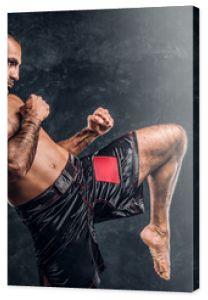 Professional Muay Thai boxer showing kick fighting technique. Studio photo against a dark textured wall