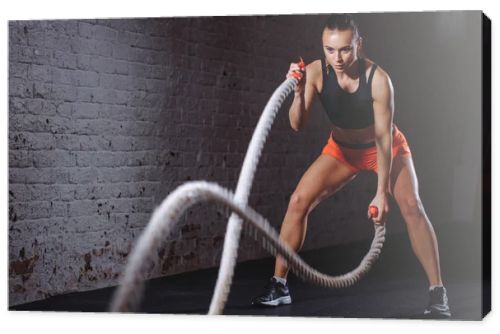 Battle ropes session. Attractive young fit and toned sportswoman training in gym