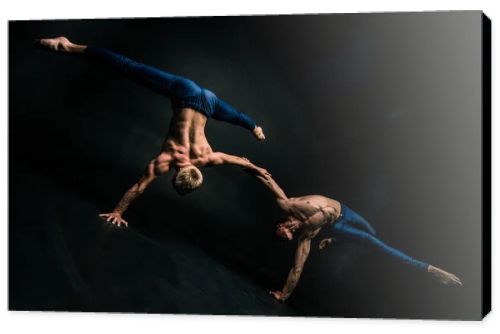 Male acrobatic duo performs a complicated balancing act on a dark background.