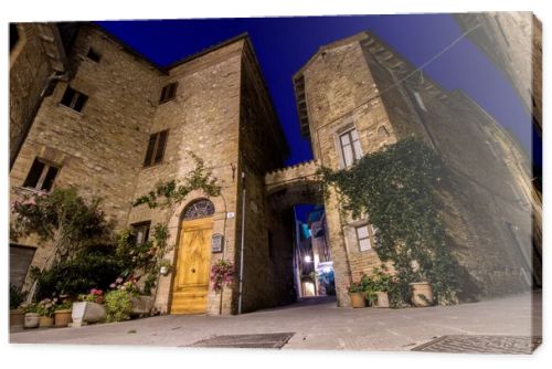 Little square of a small ancient Italian town, with brick houses, a wooden door and green and flowering plants. Journey to Tuscany and Umbria