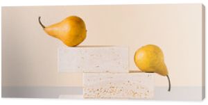 Golden yellow pears balancing on travertine marble blocks structure against gray and beige background. Creative gold summer fruit arrangement. Minimal retro styled surreal food art concept.